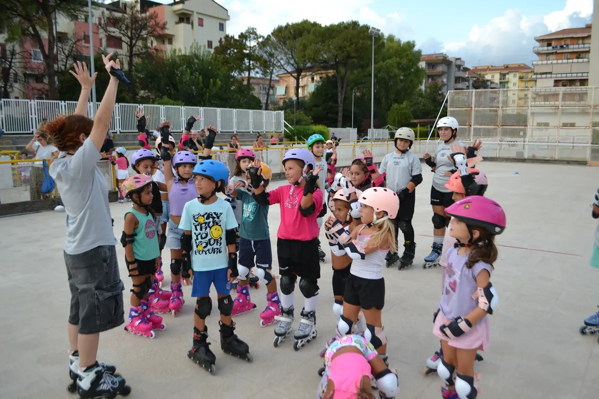 Bambini con caschi, protezioni e pattini a rotelle durante un corso di pattinaggio di ASD Sport Lab al pattinodromo di Pontecagnano, vicino Salerno