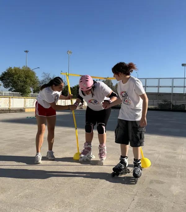 Un'atleta con il casco rosa supera un ostacolo in pista aiutata da due compagne