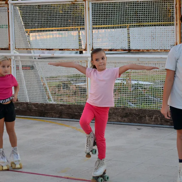 Bambina in equilibrio su un piede con i pattini a quattro ruote durante la lezione di pattinaggio artistico